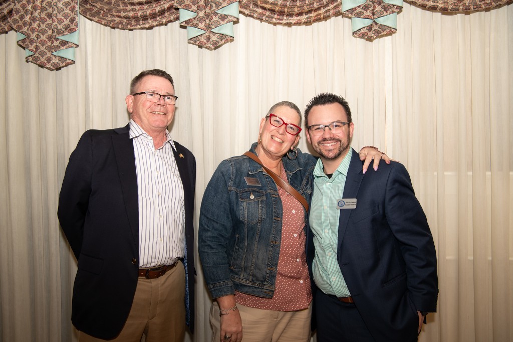 Three people posing together at a Chamber event; one wears a Board of Directors name tag.