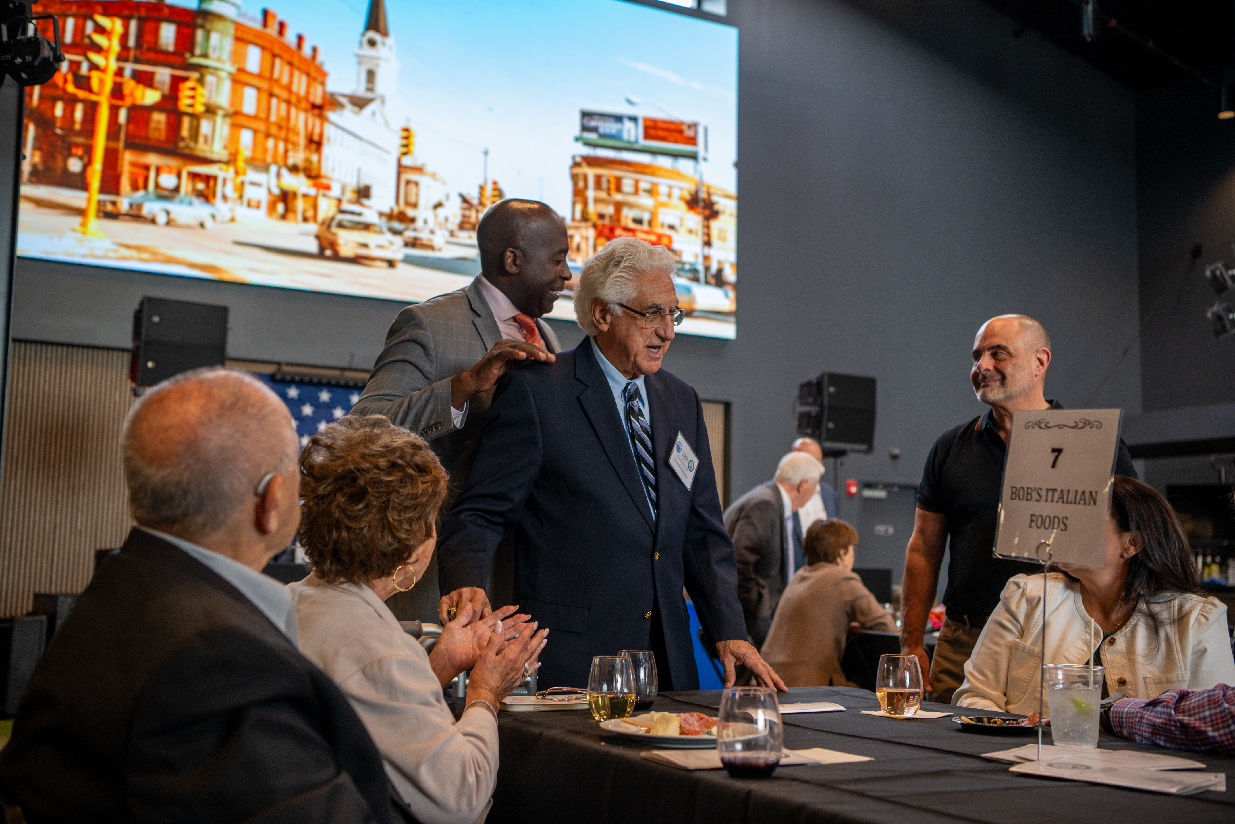 Guests at the 2025 Medford Chamber Annual Banquet mingling at a table, with a historic Medford street scene projected on the screen behind them.